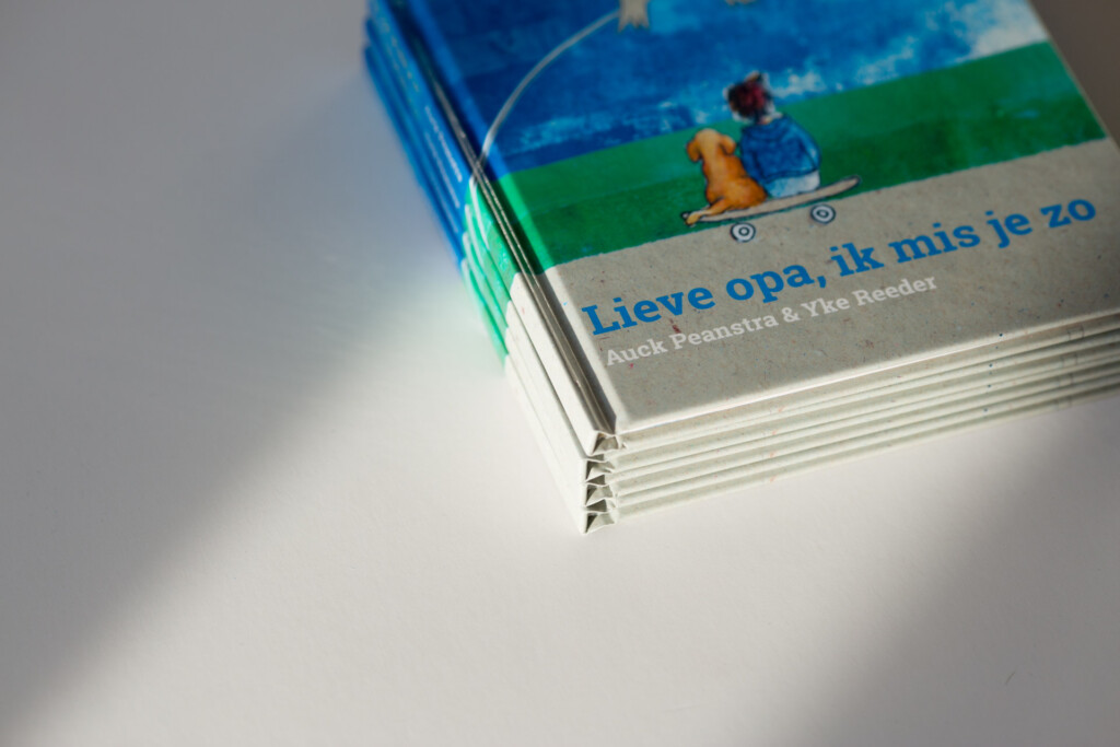 Stacked children's books with illustrated cover showing figure on skateboard, title "Lieve opa, ik mis je zo" visible on