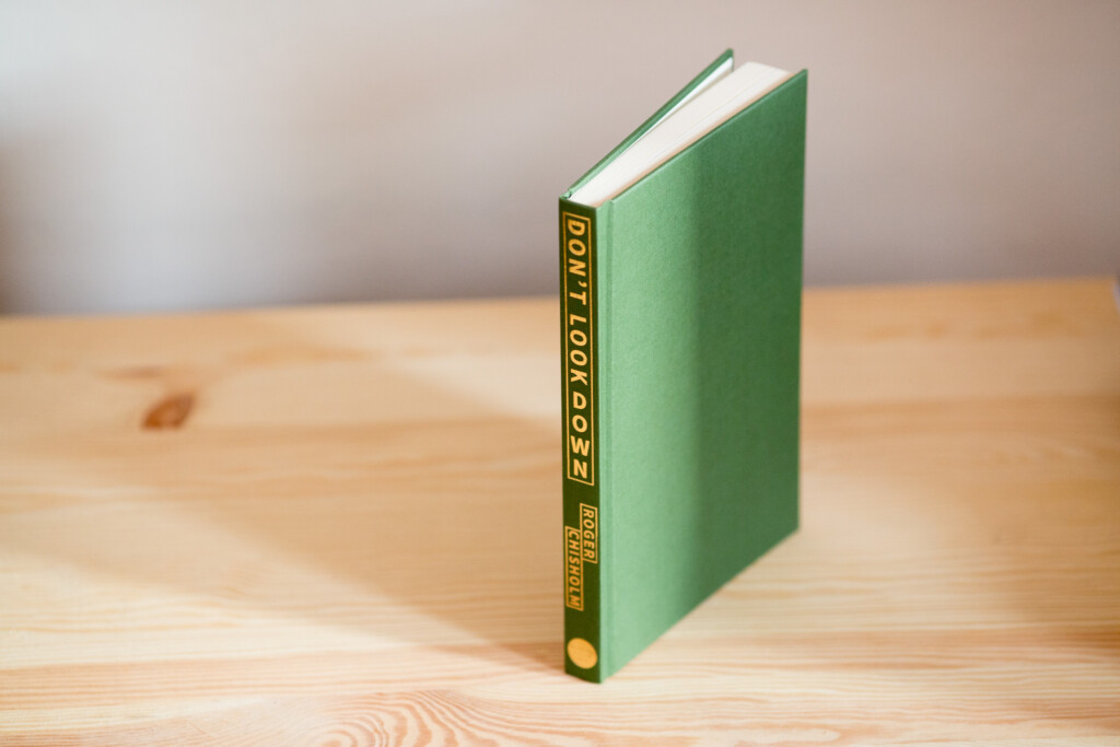 Green hardcover book with gold foil-stamped spine standing upright on wooden surface.