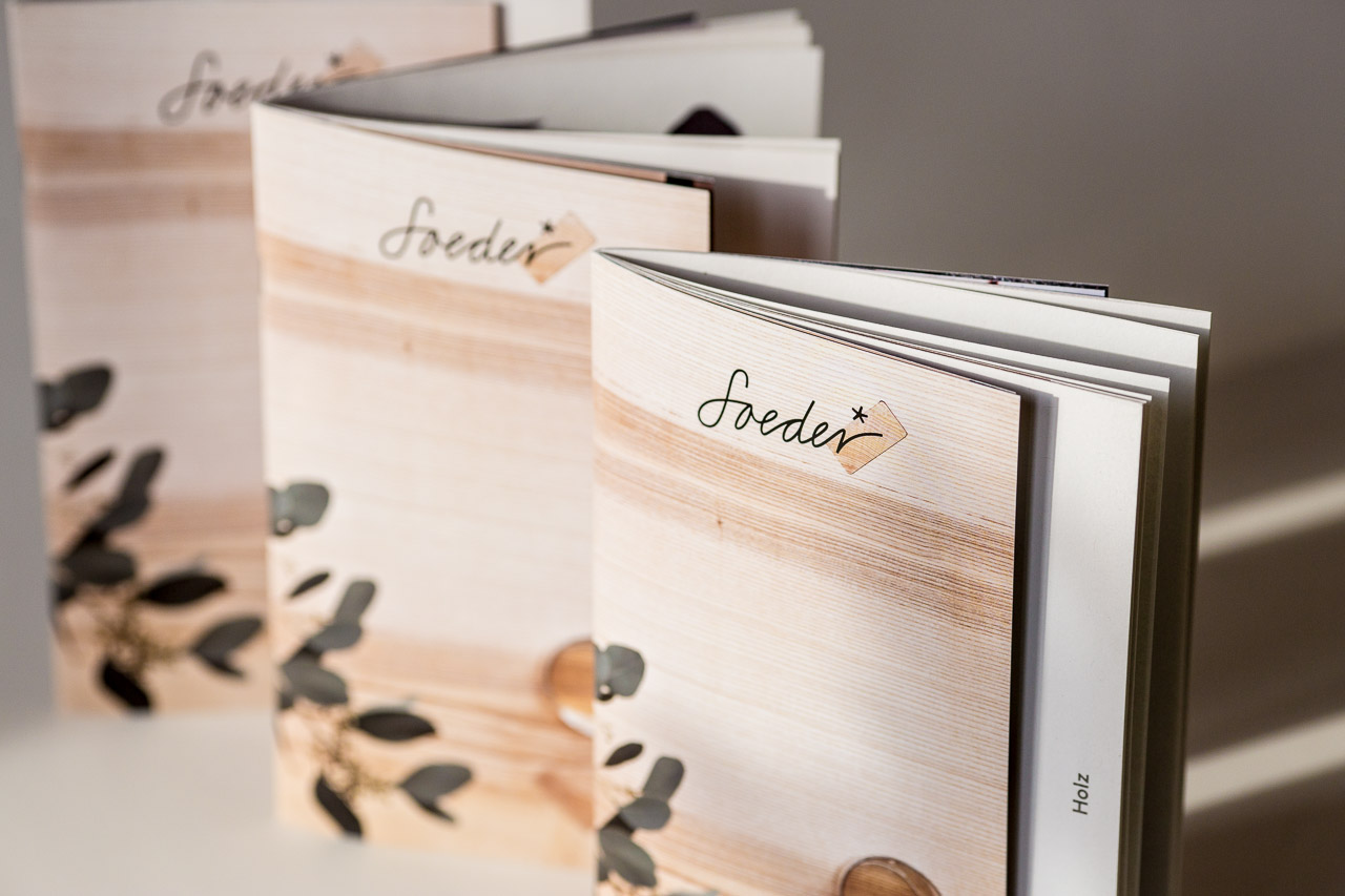 Stacked hardcover books with wooden covers featuring handwritten "Soeder" labels and eucalyptus leaf shadows cast across