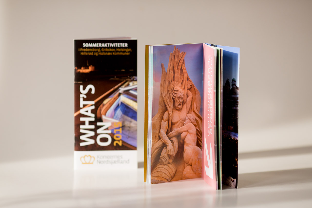 Printed brochures and catalogues fanned out, displaying coloured pages with landscape and figurative imagery, alongside a