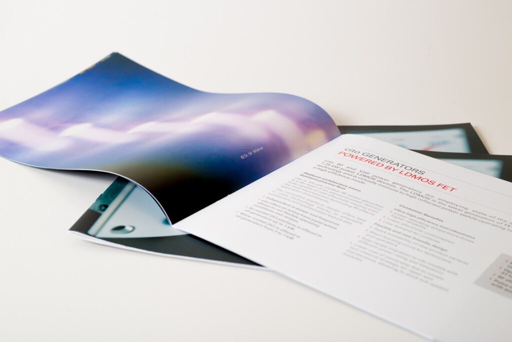 Printed brochure with blue gradient cover fanned open alongside text pages showing layout and typography details.