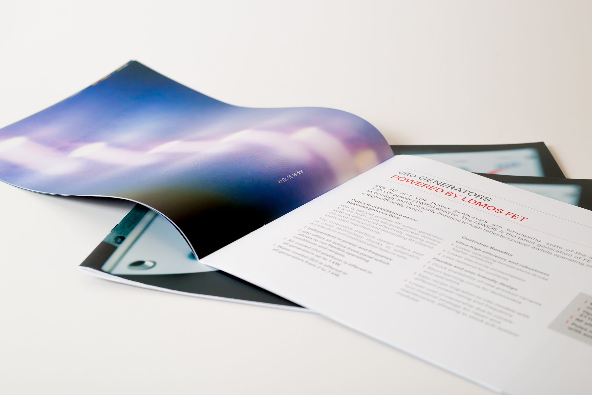 Printed brochure with blue gradient cover fanned open alongside text pages showing layout and typography details.