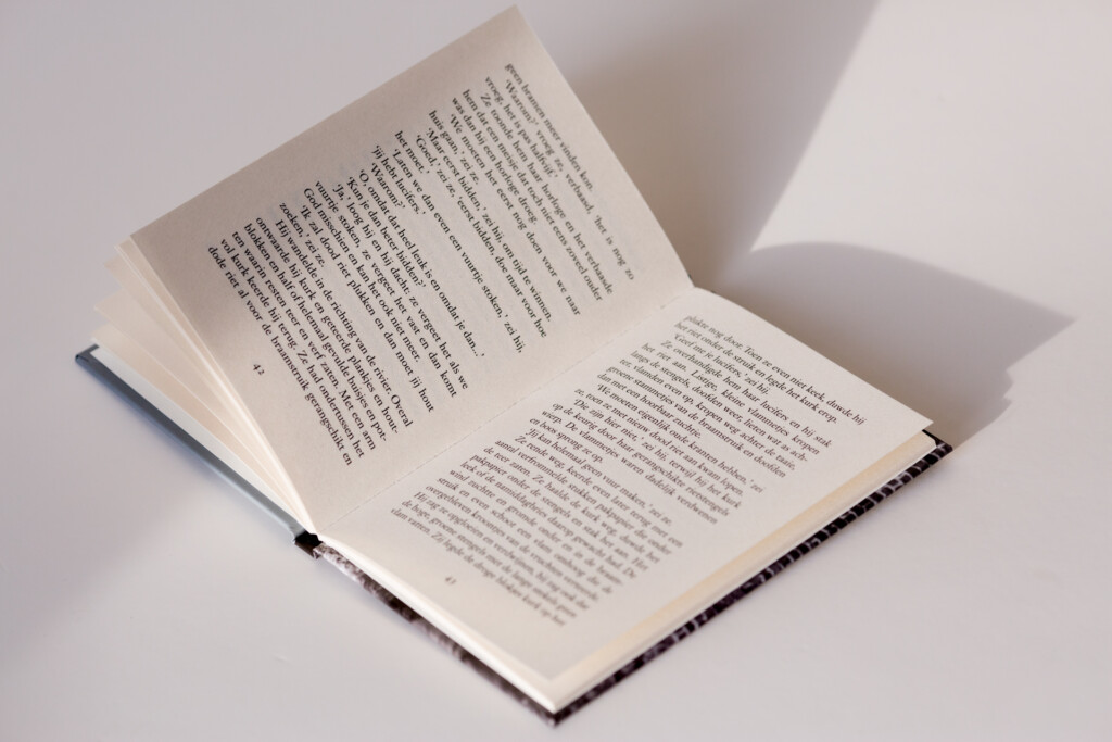 Open hardcover book with text pages and dark spine, photographed from above with shadow on white background.