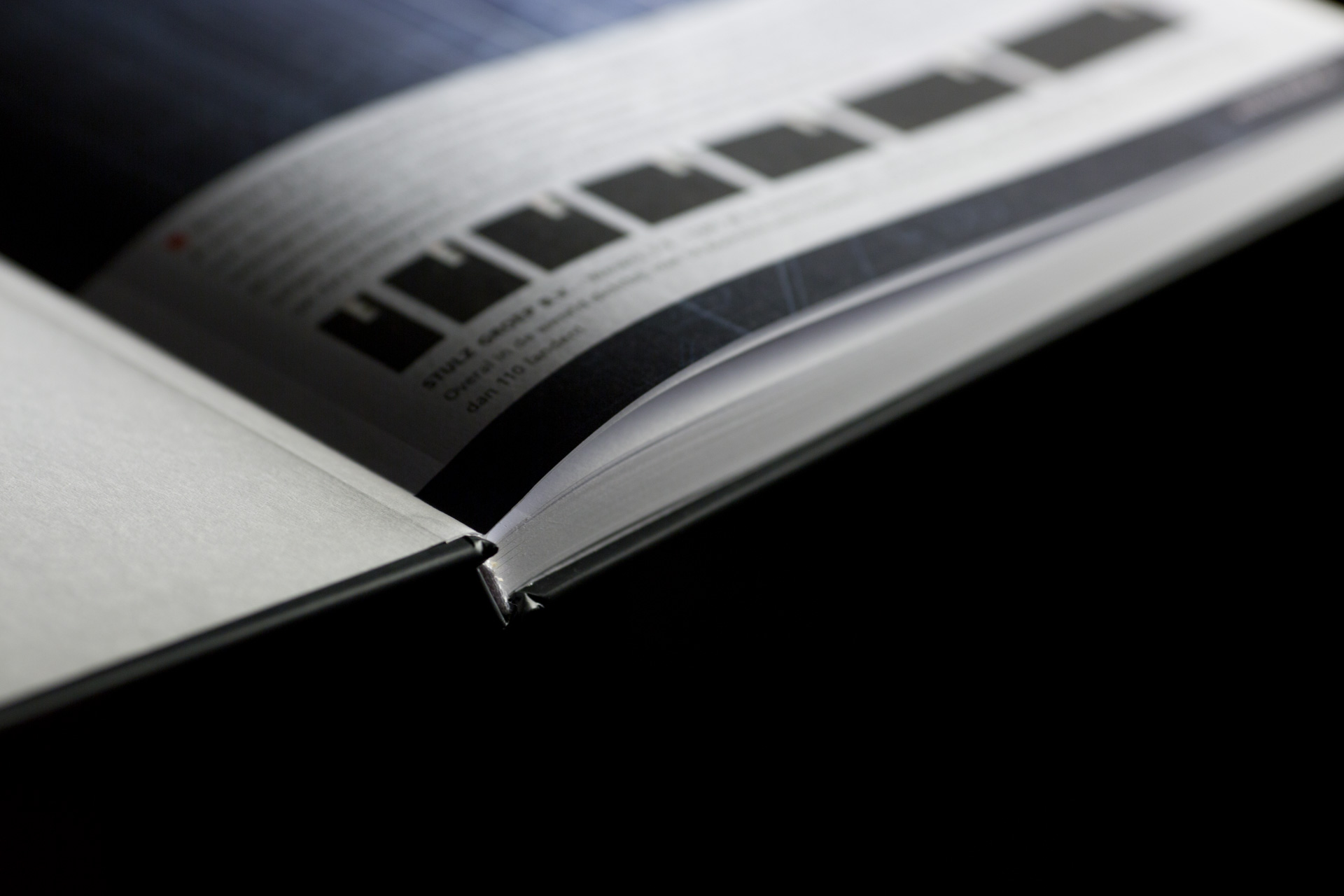 Open catalogue with pages fanned to show black and white gradient print on inner pages against dark background.