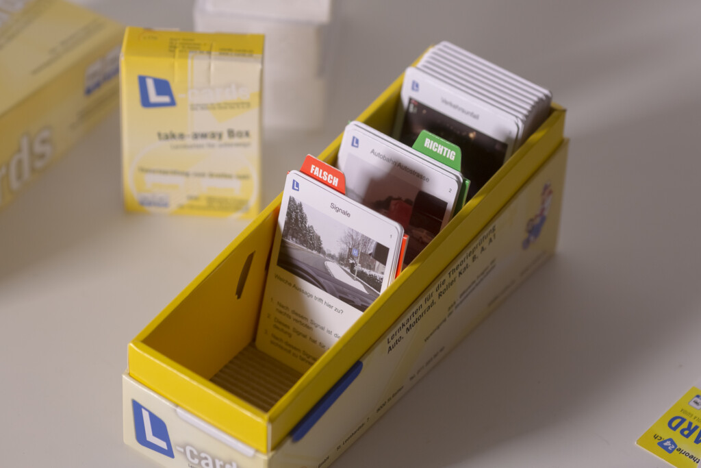 Yellow takeaway box containing compartmentalised learning cards with various subjects and coloured category tabs.