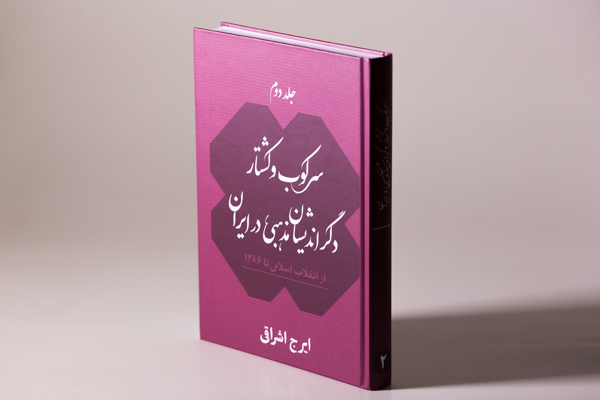 Magenta hardcover book with Arabic text and geometric dark shape on cover, displayed at angle against neutral background.