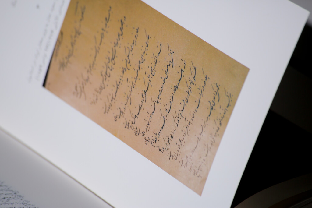 Aged manuscript page with handwritten text displayed on white mount, shown at an angle.
