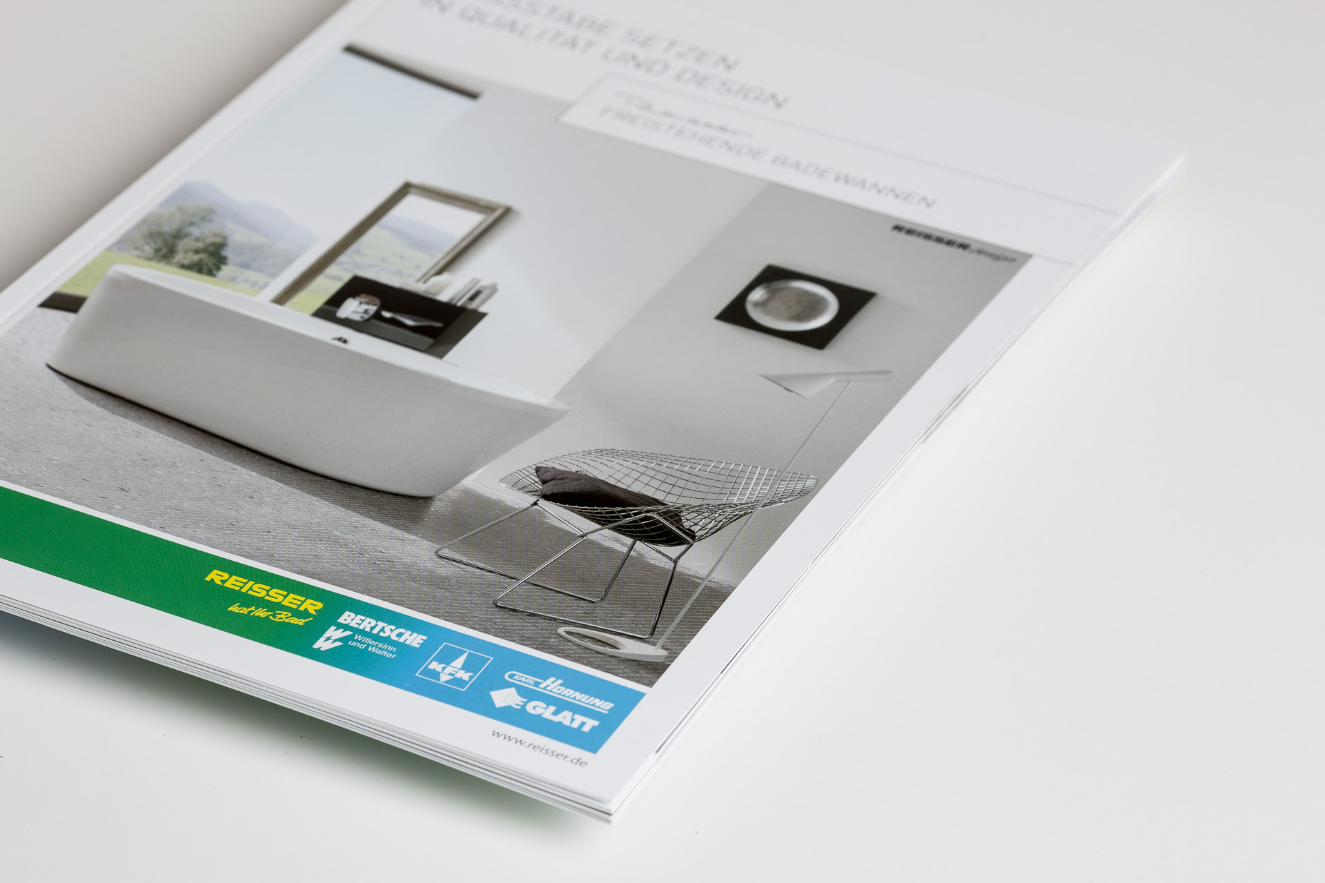 Printed catalogue showing interior spread with framed artwork mockups and chair design, displayed on white surface with