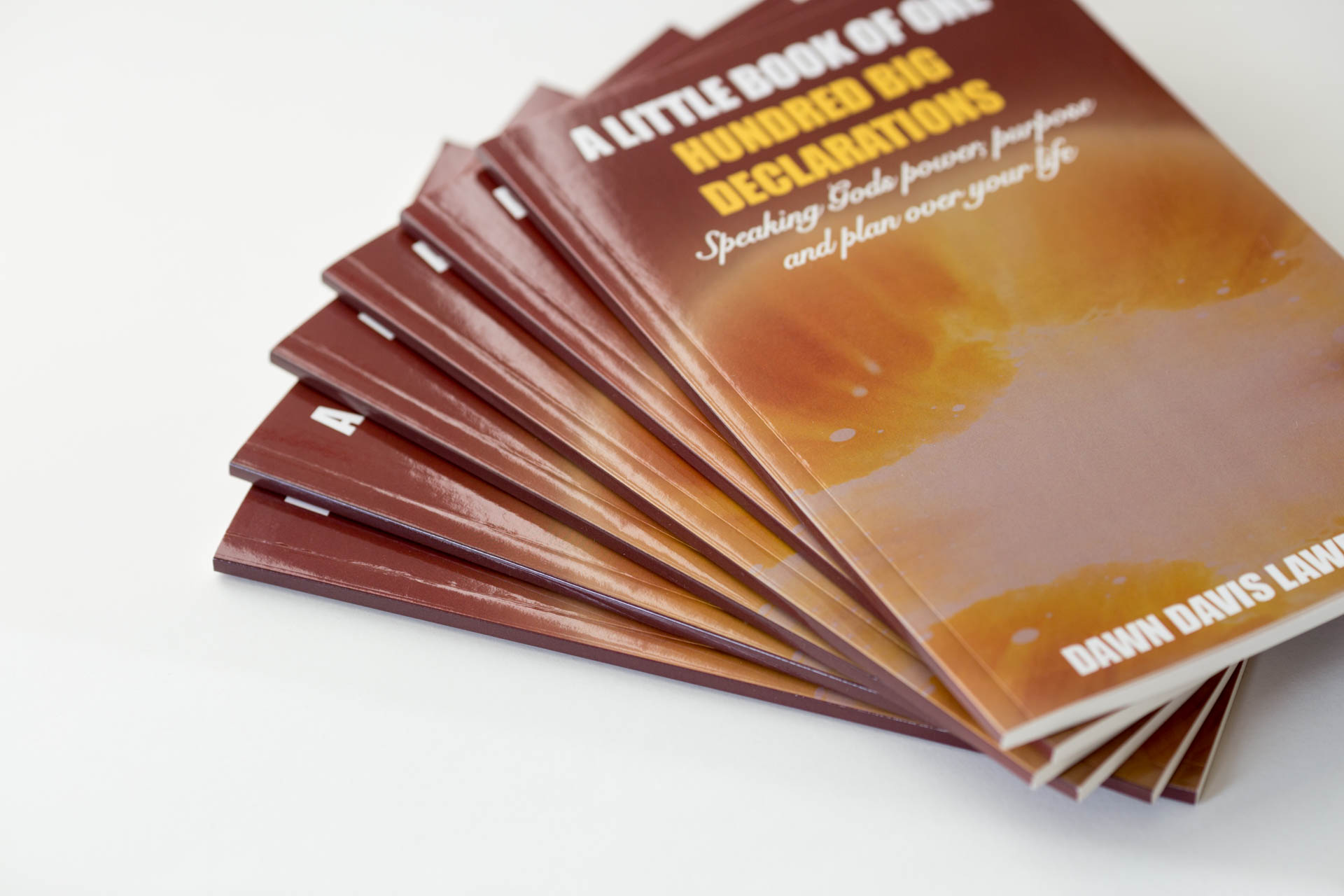 Stack of burgundy hardcover books fanned out, showing cover with gold foil stamped text and amber gradient image, against