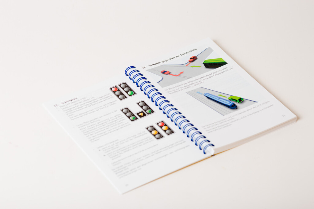 Open spiral-bound catalogue with blue wire binding, showing product pages with photographs of coloured pencils and chocolate
