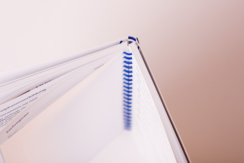 Open wire-o bound book showing blue spiral binding and white pages against a pink background.