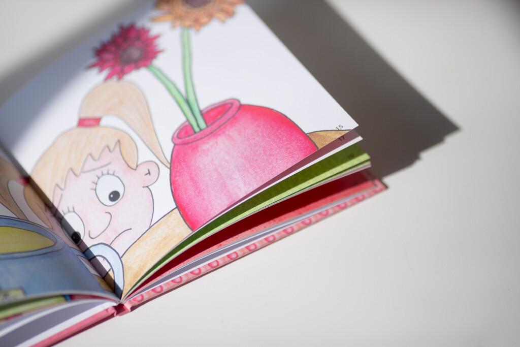Open hardcover children's book showing an illustrated spread with a character's face and a pink flower with green stem.