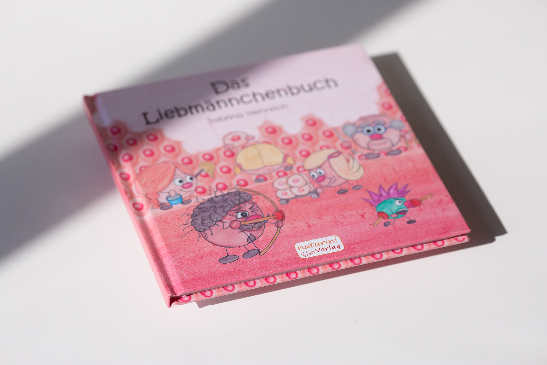 Hardcover children's book with pink cloth cover featuring illustrated characters and flowers, shown at an angle with shadow