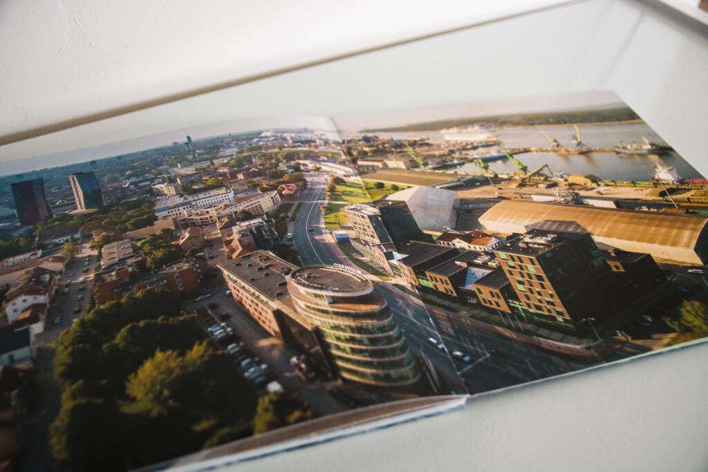 Aerial photograph printed across an open spread of a hardcover book, showing a cityscape with curved modern buildings