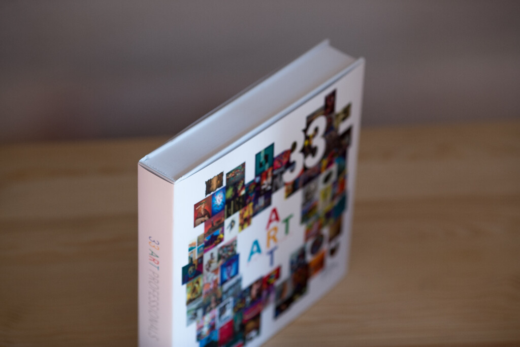 White hardcover art book with thumbnail grid design on cover, spine visible against wooden surface.