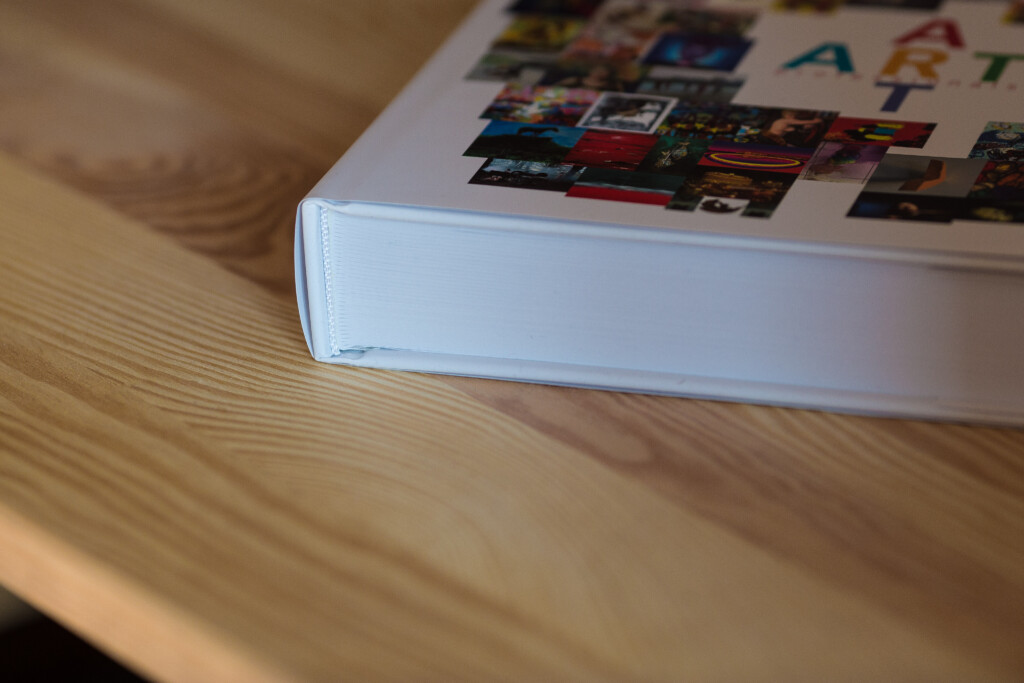 White hardcover art book with photograph collage on cover, spine detail visible on wooden surface.