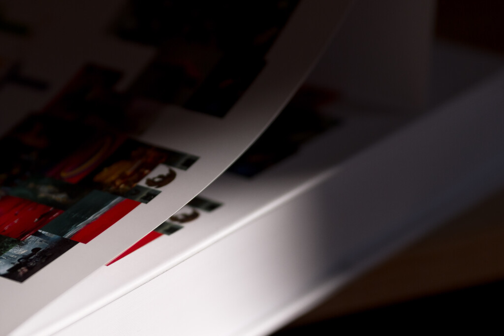 Printed art books fanned out, showing pages with red design element and photographic images on cover and spreads.
