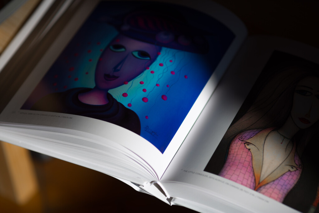 Hardcover art book open to a spread showing an abstract portrait with blue and purple tones and colourful dots, with a