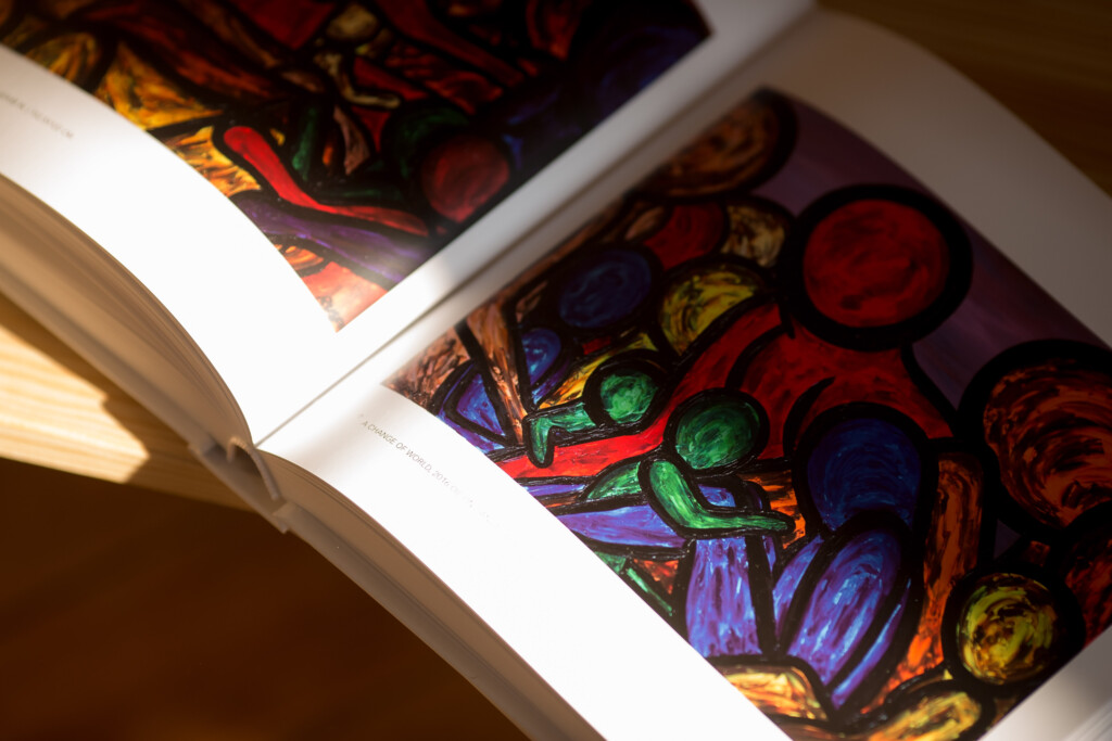 Open art book showing colourful stained glass window designs with bold reds, blues, greens and yellows across facing pages.