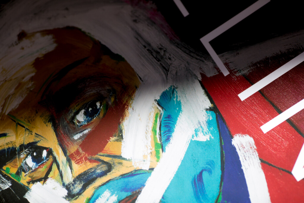 Closeup of printed album cover featuring abstract portrait with bold yellow, red, and blue colours and white graphic lines.