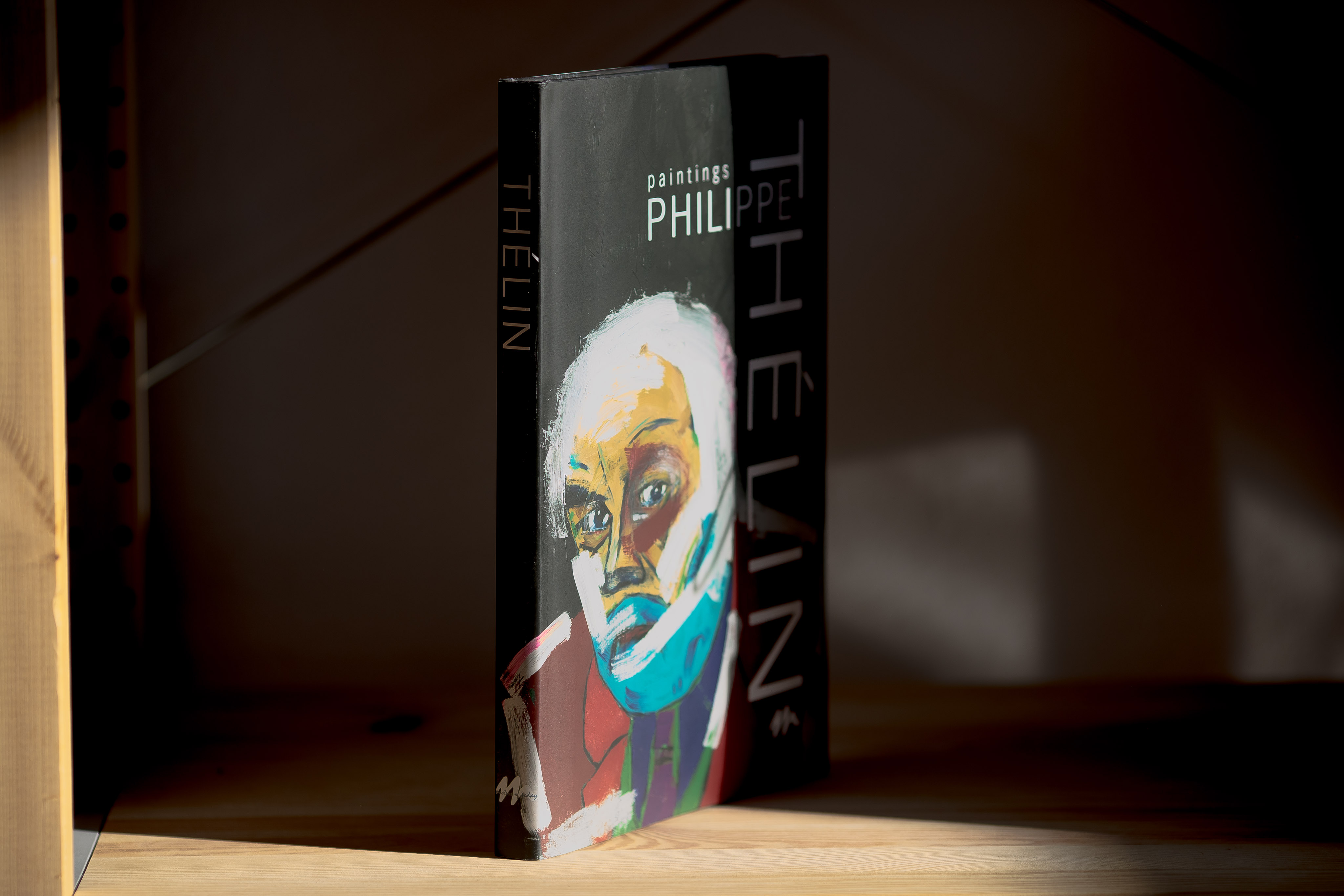 Hardcover book with portrait illustration featuring white hair and blue face paint on black cover, displayed upright on