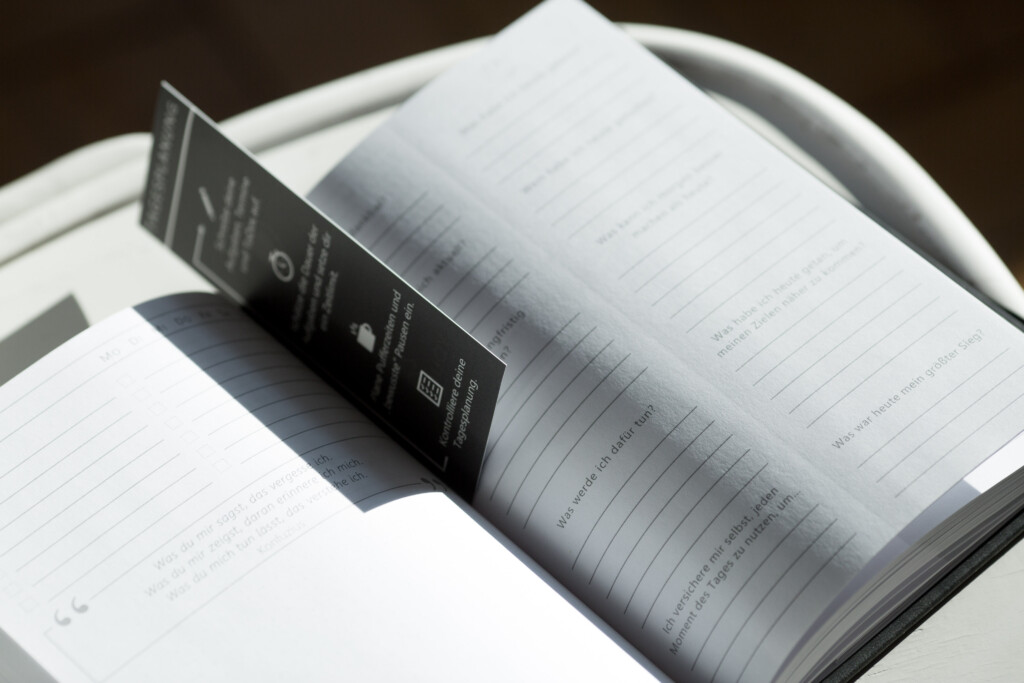 Open hardcover book with ruled pages and black bookmark ribbon against dark background.