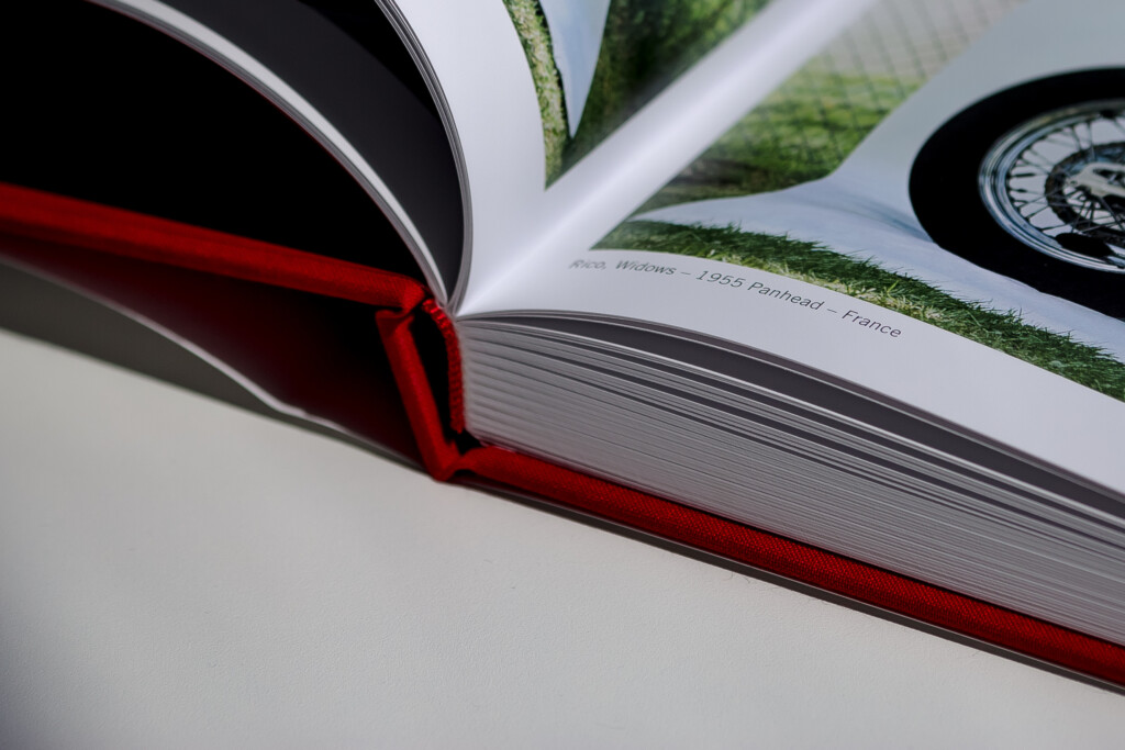 Open hardcover catalogue with red ribbon bookmark and glossy laminated cover featuring landscape photography.