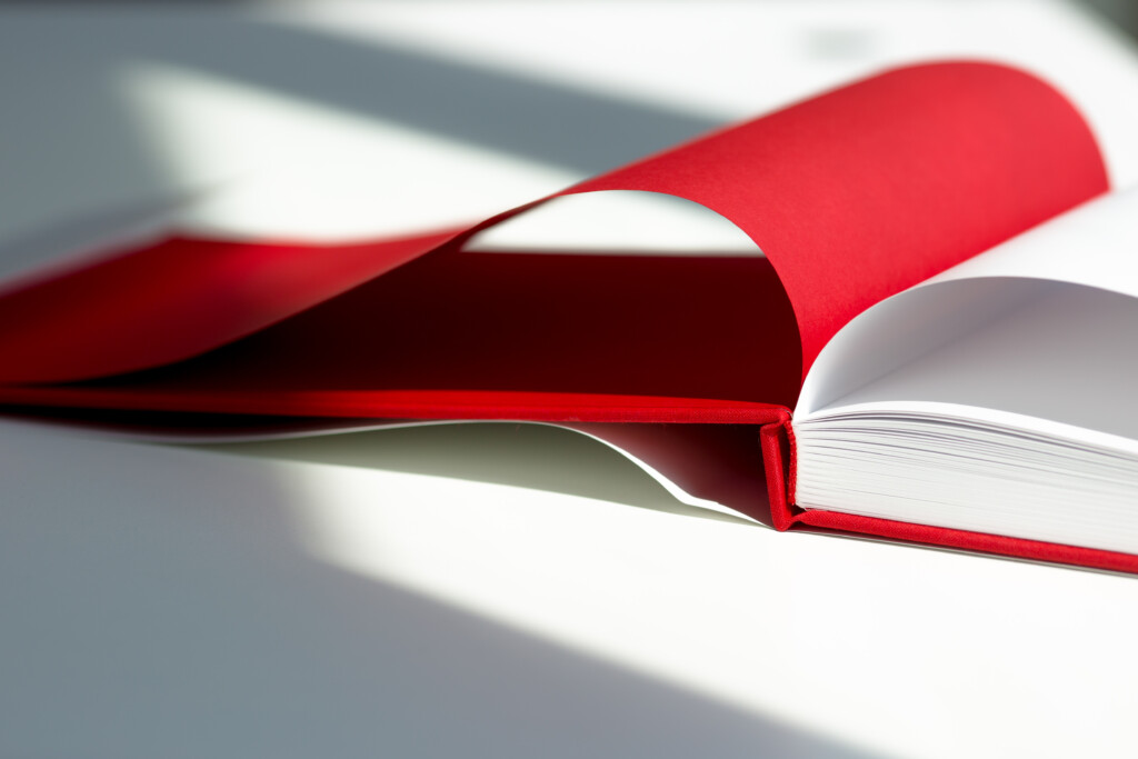 Hardcover catalogue with red cover and white pages, open to show binding detail.