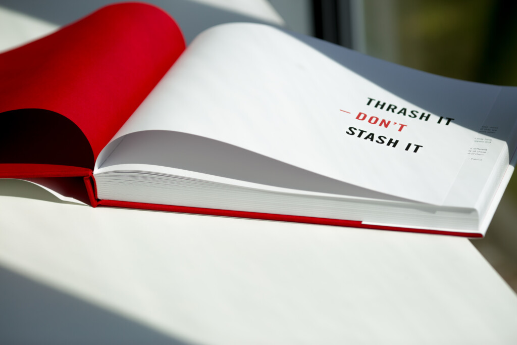 Open hardcover catalogue with red cloth binding, pages showing text reading "Thrash it, Don't, Stash it