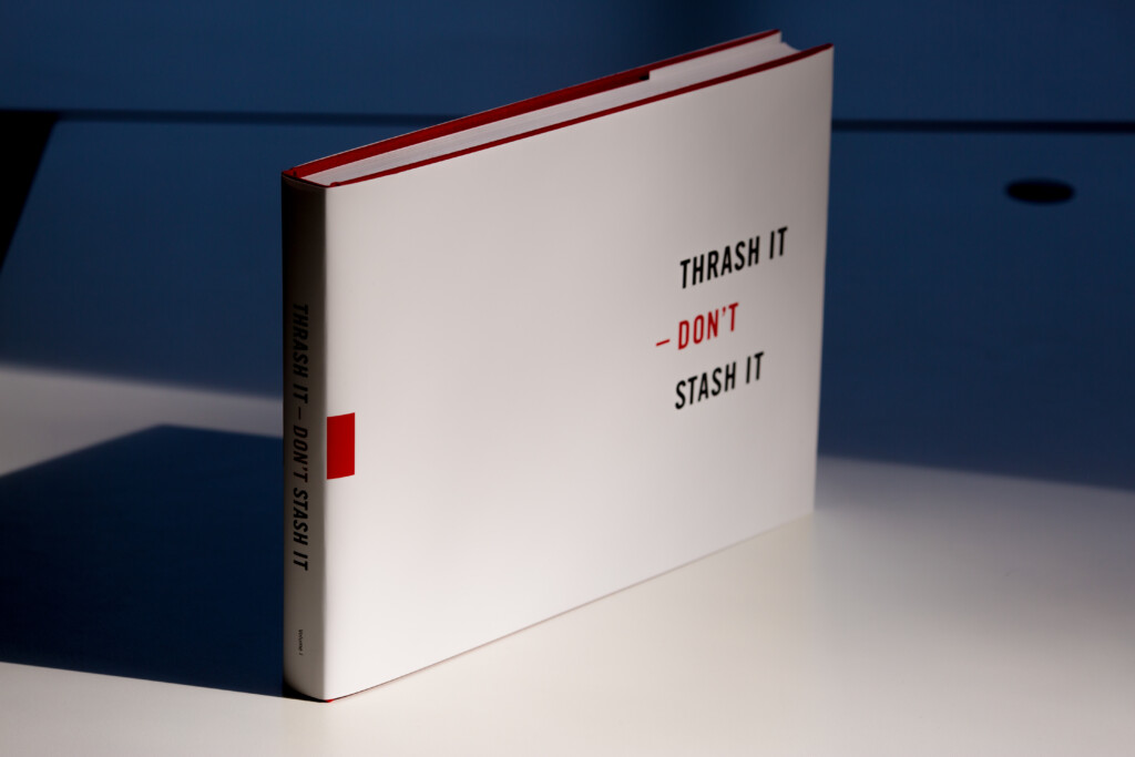 White hardcover book with red spine and trim, titled "Thrash it Don't Stash It" on cover.