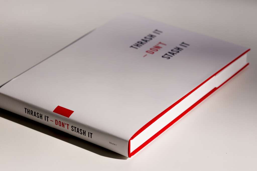 Hardcover book with white cover, red spine and red geometric line details, titled "THRASH IT - DON'T STASH IT" on spine and