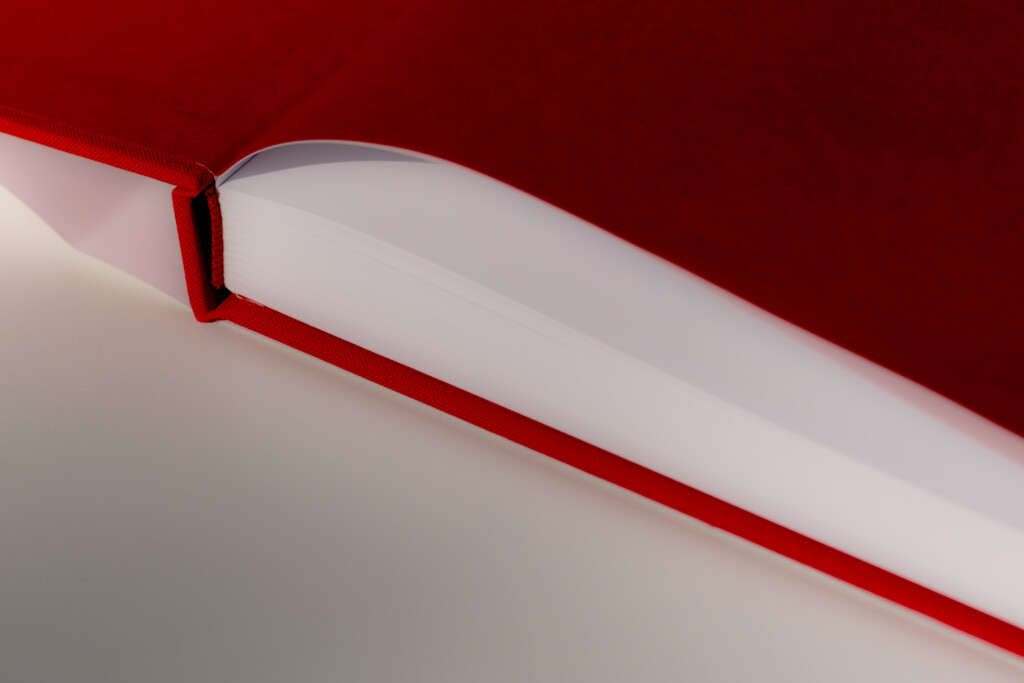 Close-up of hardcover catalogue spine and binding with red cloth covering and white pages against red background.