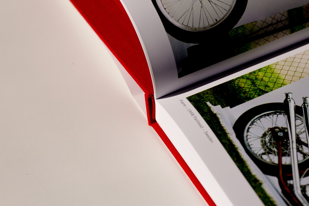 Hardcover catalogues fanned out showing open spreads with bicycle imagery and green mesh details, with red ribbon accent