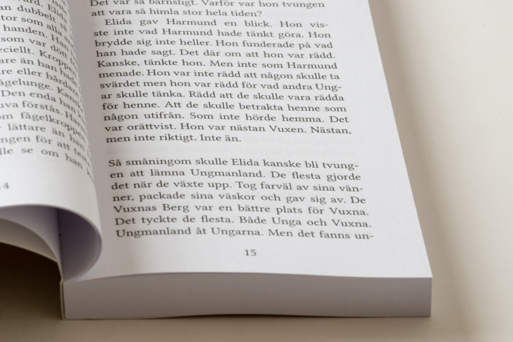 Open book showing Swedish text on page 15, with a finger pointing to a paragraph, displaying sewn binding and cream-coloured
