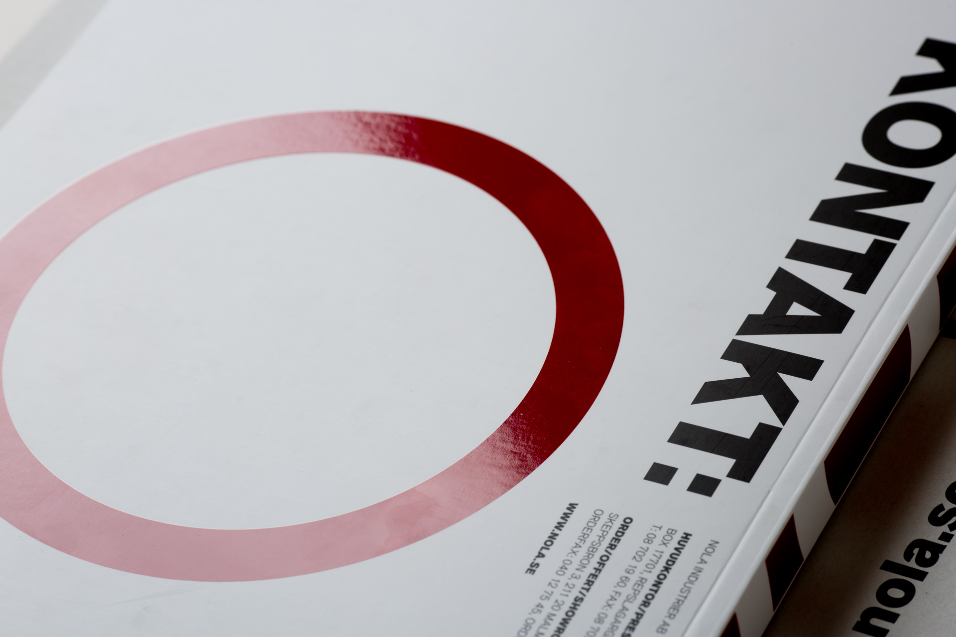 Nola product catalogue with red oval design element on white cover and visible text on spine.