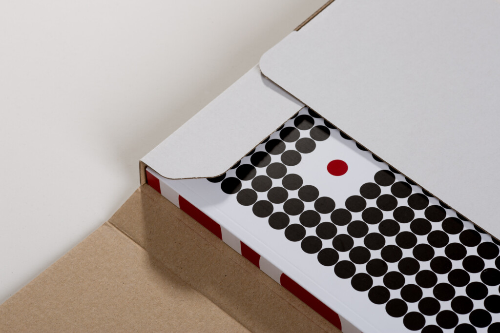 Printed product catalogue with black circular dots pattern and one red dot, partially visible inside open white cardboard