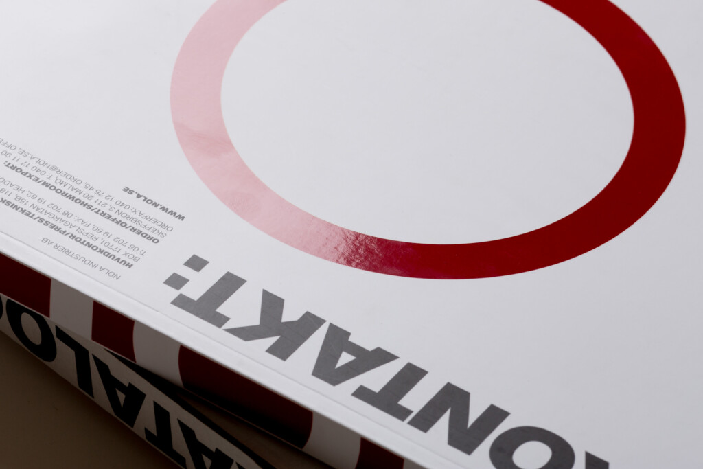 Corner detail of a printed catalogue with pink and burgundy curved graphic design and partial text visible on the spine.