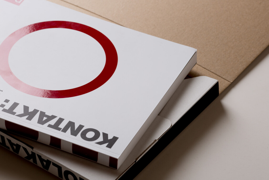 Printed product catalogue with red circular design on white cover, stacked with other catalogues.