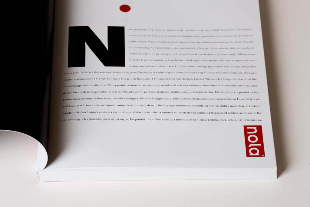 Nola product catalogue open on white background, showing large black letter N on left page with red dot above and small red