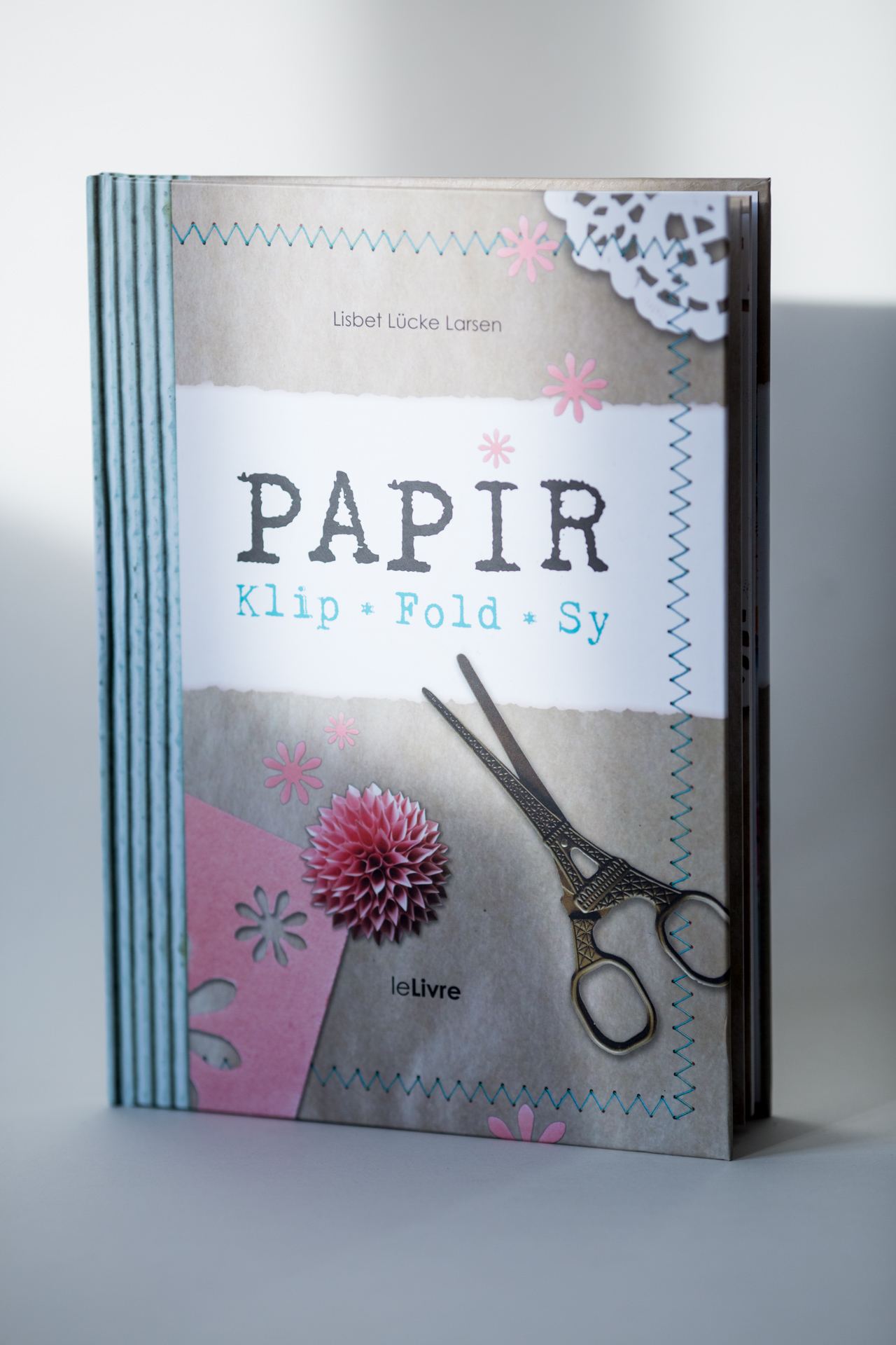 Hardcover sewn book titled "PAPIR Klip Fold Sy" with pink floral design, white lace detail, and black scissors on cover.