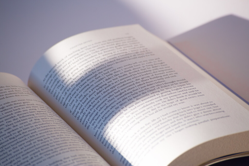 Open paperback book with sunlight illuminating the pages, showing printed text across the spread.