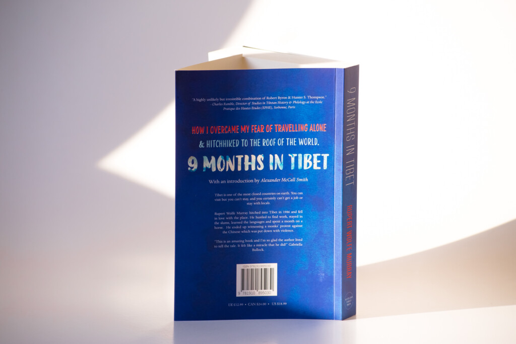Paperback book with blue cover titled "9 Months in Tibet" describing overcoming fear of travelling alone, photographed