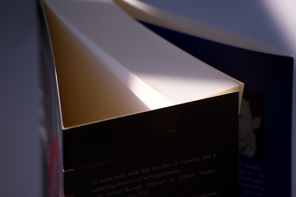 Paperback book with white top edge and black cover, photographed at an angle with light illuminating the pages inside.