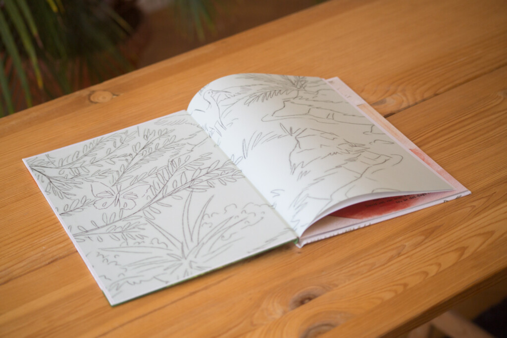 Hardcover children's book with illustrated botanical line drawings on open pages, displayed on wooden table.