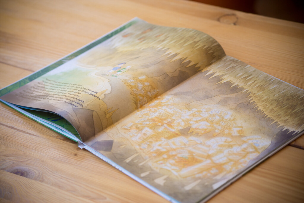 Open hardcover children's book with illustrated pages showing textured artwork in gold and cream tones on wooden surface.