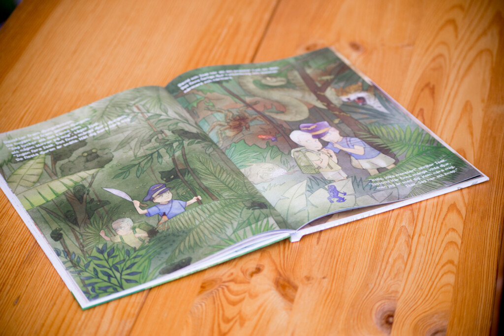 Hardcover children's book opened to show illustrated pages with woodland creatures and foliage on wooden surface.