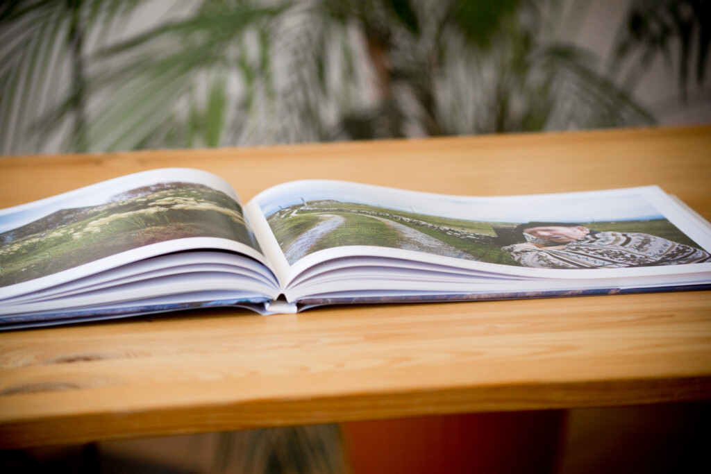 Open hardcover book displaying aerial landscape photographs on wooden table with potted plant in background.