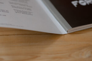 Open softcover book with linen spine on wooden surface, showing pages with text and binding detail.