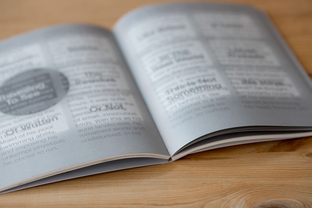 Open softcover book with Swiss binding on wooden surface, showing text pages with visible spine stitching.