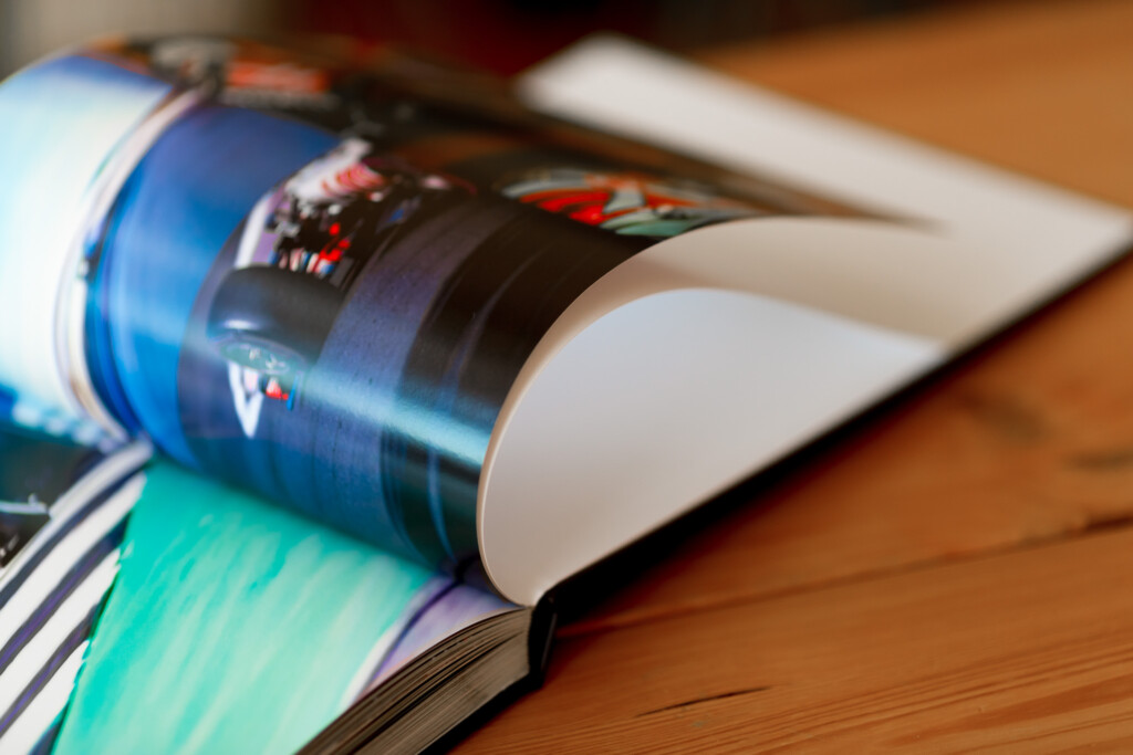 Printed photo album with glossy laminated cover, fanned open to show colourful pages on wooden surface.